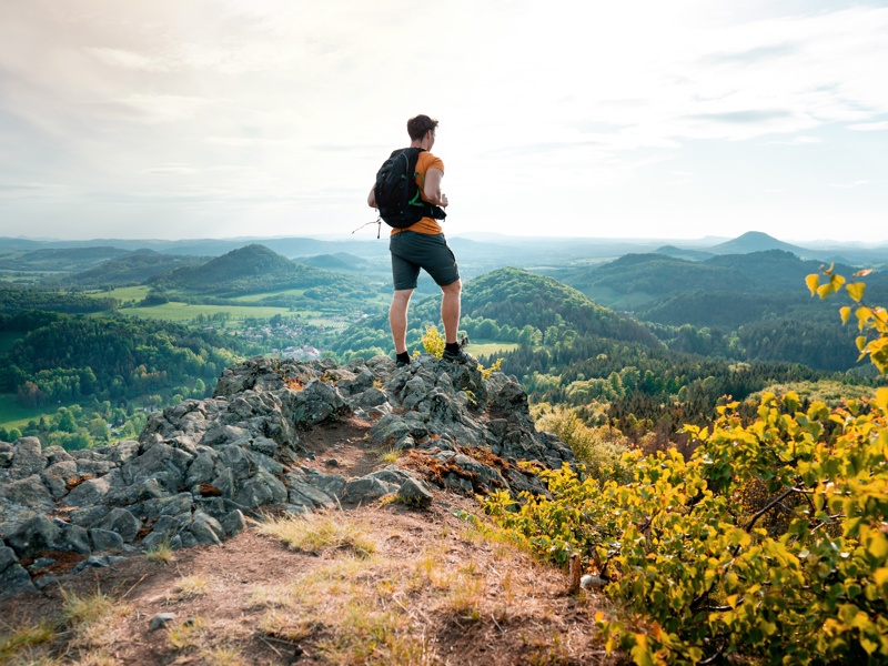 Man hiking on top of a rocky mountain peak. Steep cliff, rocky part of path with view into distance. Scenic landscape of Lunation Mountains, Czech Republic