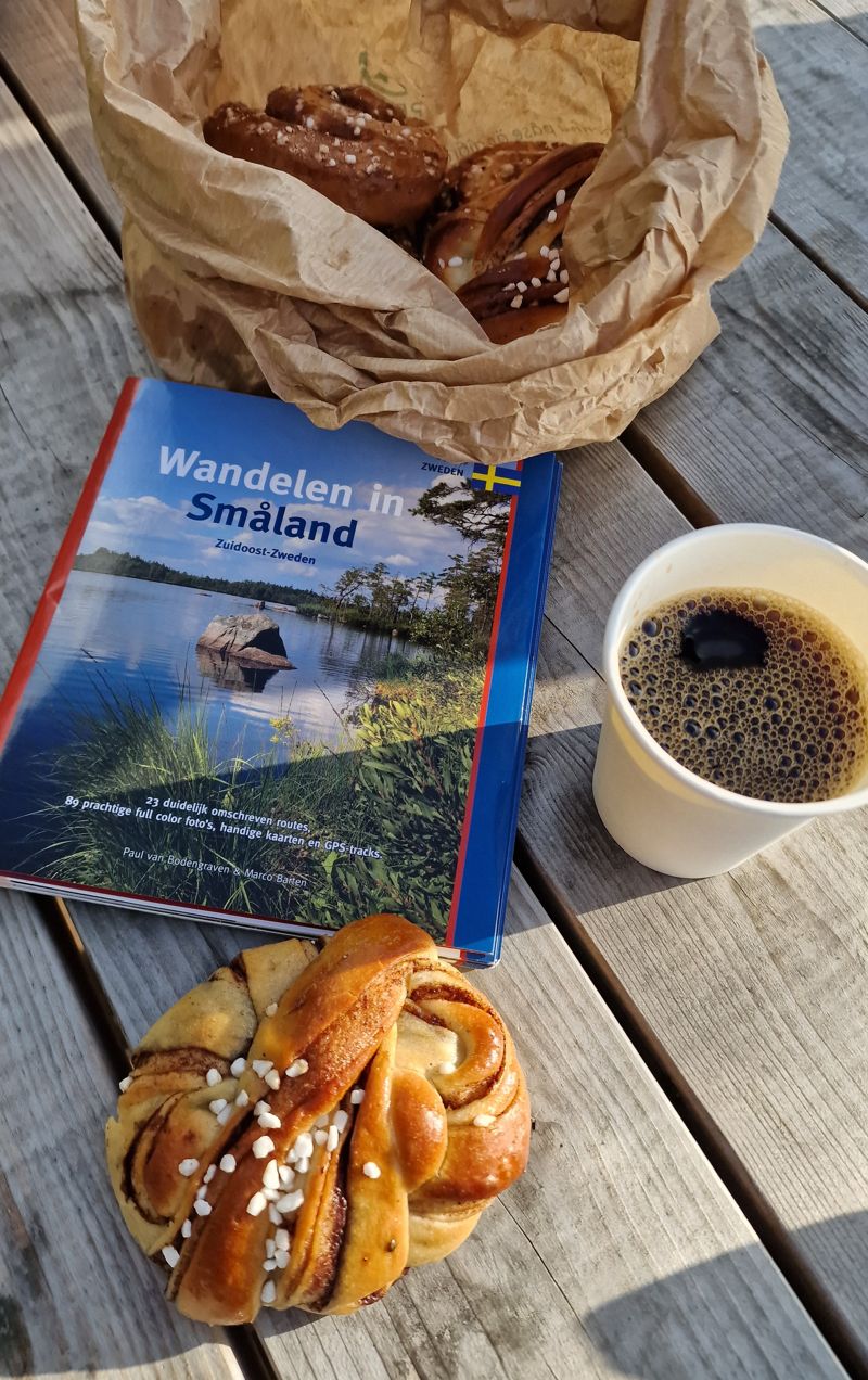 Een fika met kaneelbroodje en wandelgids 'wandelen in Smaland'.